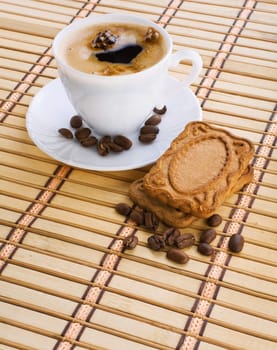 cup of capuchino with coffee beans and cookie on a mat