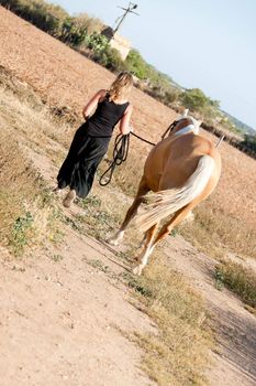 young woman walking away in sunset with horse summertime