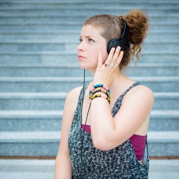 beautiful stylish modern young woman listening to music in the city