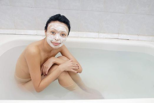 Smiling model with beauty mask sitting in the bath