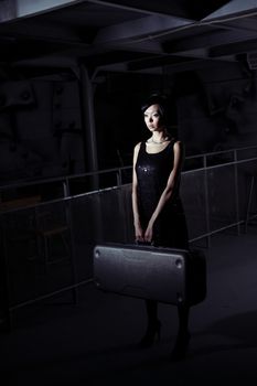 Small brunette lady holding big suitcase in the dark airport terminal