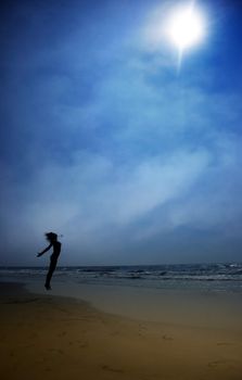 Silhouette of the jumping lady at the summer beach. Artistic colors and darkness added