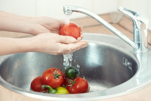 Hands of woman washing vegetables at her kitchen