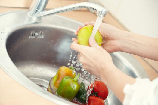 Hands of woman washing vegetables at her kitchen