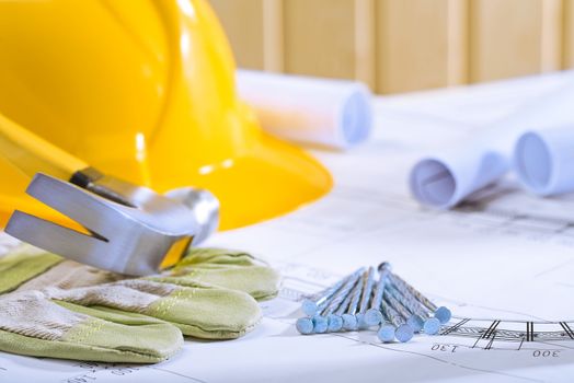 hammer on glowe and nails with helmet on blueprints