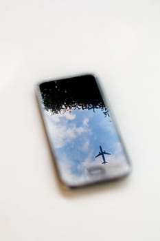 plane reflection on mobile phone with blue sky and tree