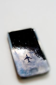 plane reflection on mobile phone with blue sky and tree