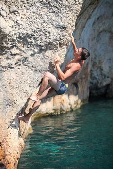 Deep water soloing, male rock climber on cliff