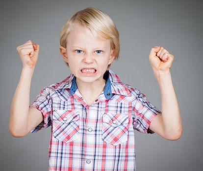 A frustrated and angry looking young boy with fists clenched and pulling a face. Isolated on white.