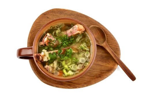 Vegetable Soup with Cabbage, Greens and Smoked Pork Ribs in Brown Bowl with Wooden Spoon on Wooden Plate. Top View