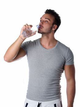 Fit and handsome young man drinking water from plastic bottle, isolated on white