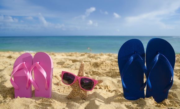 Flip flops and starfish with sunglasses on sandy beach with adult and child in the ocean on background