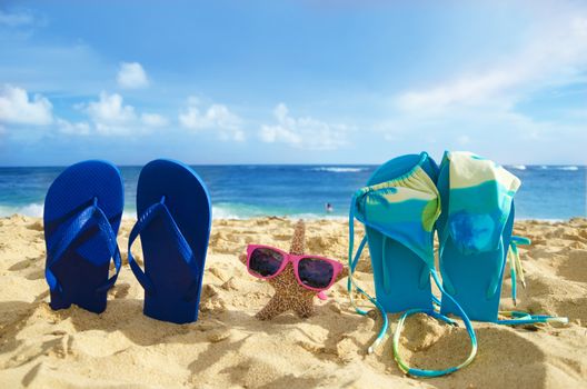 Flip flops with bikini and starfish with sunglasses on sandy beach with adult and couple in the ocean on background