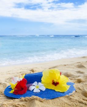 Woman's hat with tropical flowers on sandy beach in Hawaii, Kauai