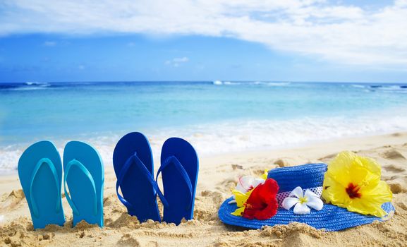 Flip flops and woman's hat with tropical flowers on sandy beach in Hawaii, Cauai