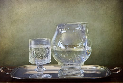 Crystal glass and  glass pitcher with sparkling mineral water on silver tray against a grunge background