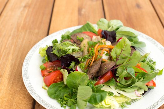 Salad with fried rabbit liver and fresh vegetables on a wooden table.