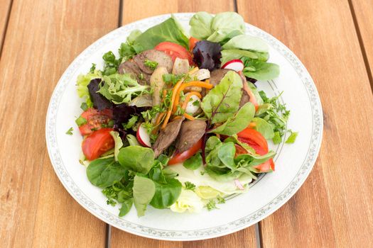 Salad with fried rabbit liver and fresh vegetables on a wooden table.