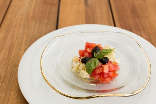 Fresh mozzarella and tomatoes tartar in glass plate on a wooden table.