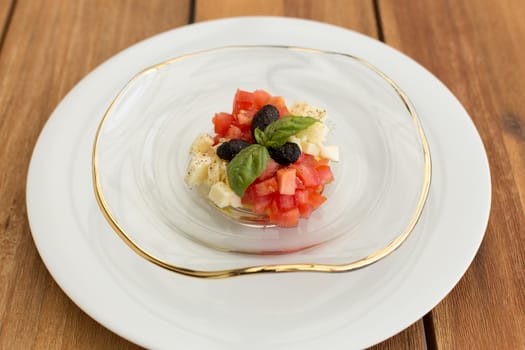 Mozzarella and tomatoes tartar in glass plate on a wooden table.