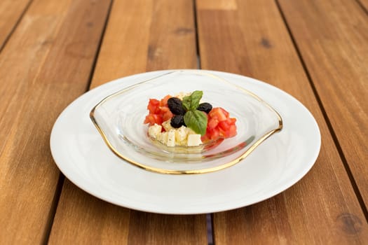 Caprese mozzarella and tomato tartar in glass plate on a wooden table.