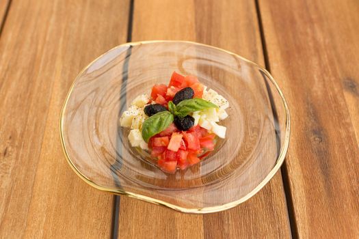 Caprese tartar in soup glass plate on a wooden table.