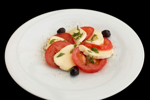 Fresh caprese salad in white plate on a black background.