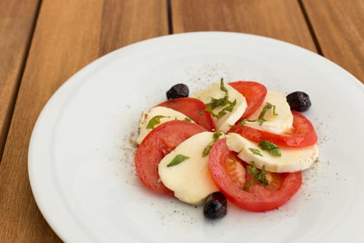 Mozzarella and tomato salad in white plate on a wooden table.