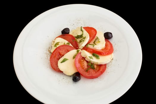 Delicious caprese salad in a white plate on a black background.