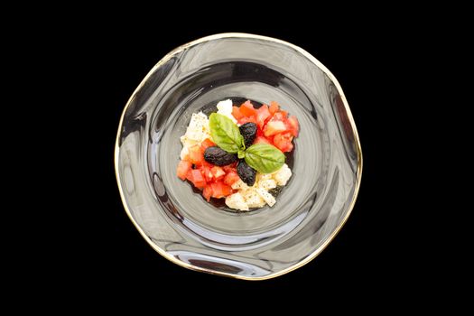 Tomatoes and mozzarella tartar in soup glass plate on a black background.