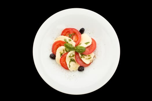 Fresh tomatoes, mozzarella salad in white plate on a black background.