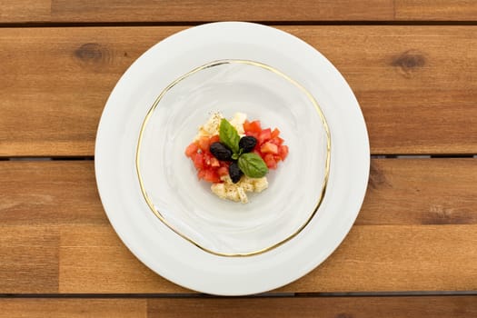 Fresh caprese tartar in glass plate on a wooden table.