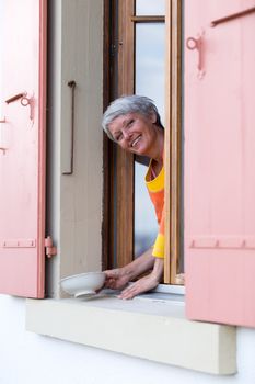 Happy modern senior woman with white hairs looking from the window.