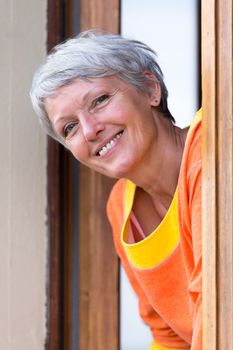 Smiling modern mature woman with grey hairs looking from the window.