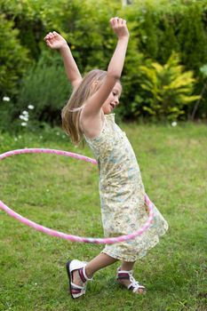 Smiling little girl playing with hula hoop in her garden.