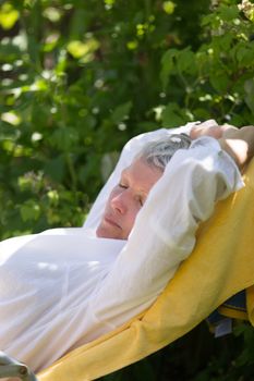 Senior woman with grey hairs sleeping on lounger in her garden.