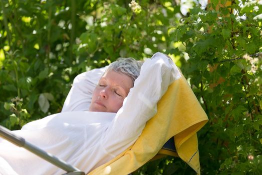 Mature woman with white hairs sleeping on lounger in her garden.