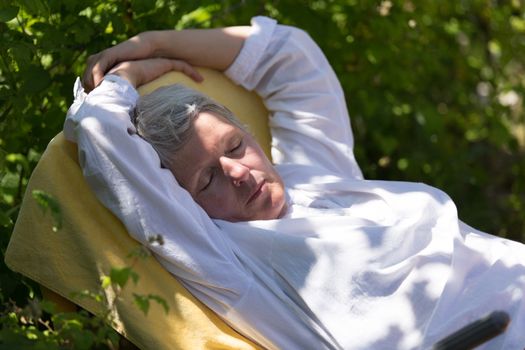Mature woman with grey hairs sleeping on lounger in her garden.