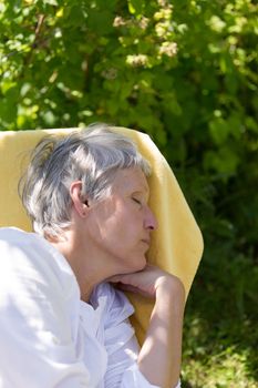 Aged woman with grey hairs sleeping on lounger in her garden.