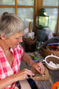 Senior woman with white hairs cutting food on wooden board.