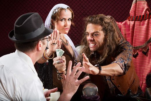 Aggressive fortune tellers taking money from man in hat