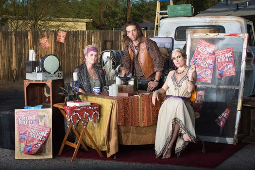 Three serious fortune tellers sitting outside at kiosk