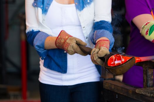 A female is blowing glass and using a wooden shaping tool to form the shape she wants the glass to end up as. The glass is hot and molten so she has to use water with the wood.