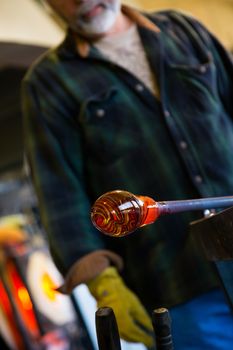 A very talented glassblower is forming and shaping glass in a studio for glass making. He is creating a fluted bowl from this piece of molten glass.