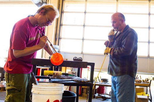Two men are working hard to create a unique art piece of molten glass. They are glassblowing at a studio in Oregon.