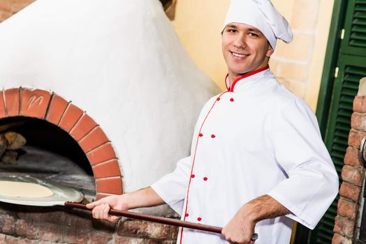 Chef puts dough in the oven for pizzas, traditional cooking