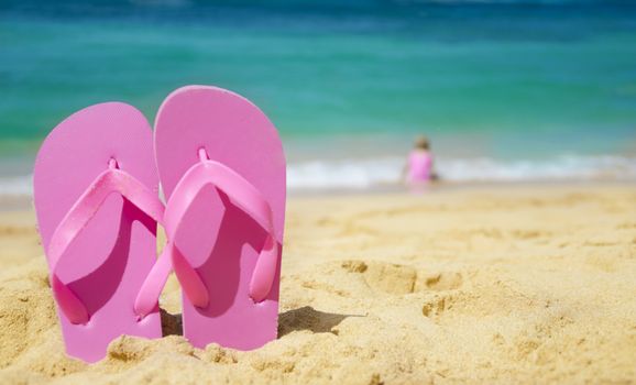 Flip flops on sandy beach with playing girl by the sea on background (Hawaii, Kauai)
