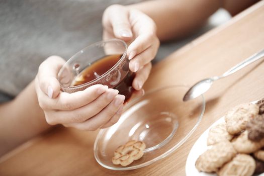 Human hands holding cup of tea with cookies