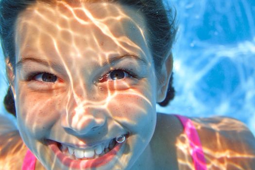 Close-up portrait of the cute girl swimming underwater and smiling