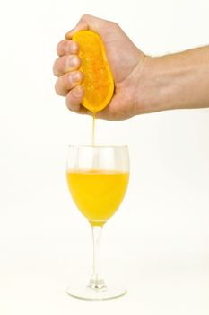 A caucasian male hand squeezes fresh juice from an orange into a glass against a white background.